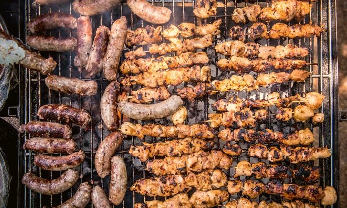 Overhead view of a charcoal grill loaded with chicken skewers and sausages