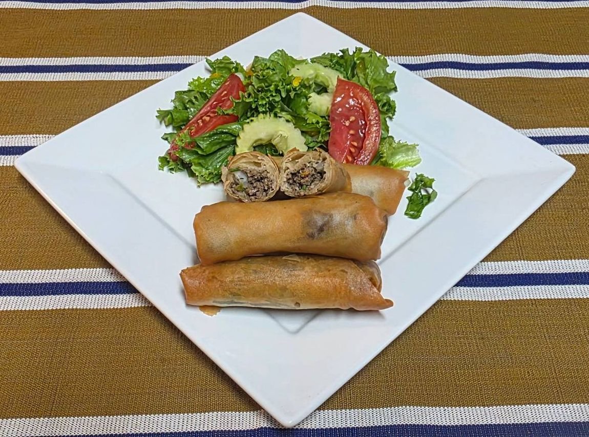 Crispy nem spring rolls, one cut open to show seasoned beef, with house salad